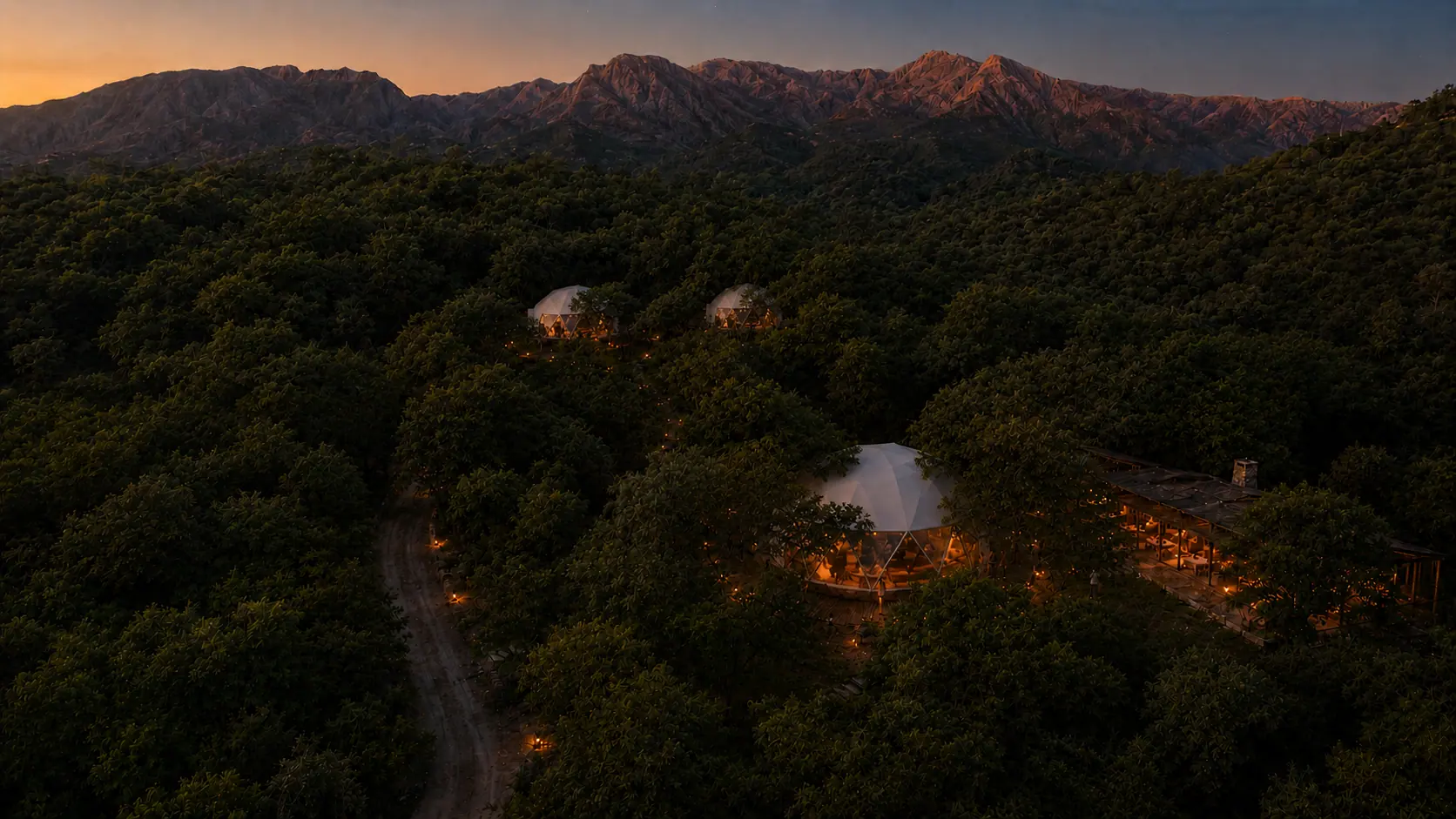 Vista aérea del desarrollo al atardecer: domos entre el monte nativo y las sierras de Traslasierra al fondo